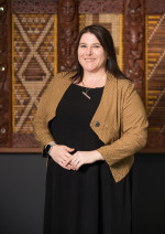 Steph Voight standing in front of a tukutuku panel looking at the camera and smiling